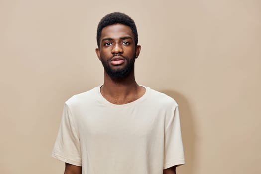 This image features a young Black male model with a calm demeanor, dressed in a simple light beige T shirt The monochromatic background enhances the focus on his confident expression, making it idea