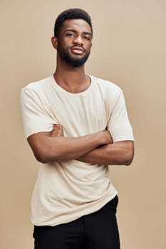 Confident young African man poses against a beige backdrop, arms crossed, expressing self assurance The image captures modern style and casual fashion perfect for lifestyle themes