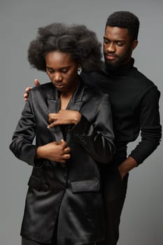 This striking image features a fashionable African couple, with one partner wearing a sleek black blazer and the other in a turtleneck, combined with a muted gray background, capturing emotions of su
