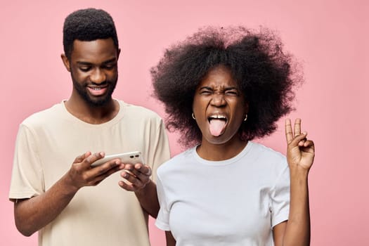 Cheerful young couple, one with a smartphone, expressing happiness and playfulness against a vibrant pink background, ideal for concepts of young love and modern relationships