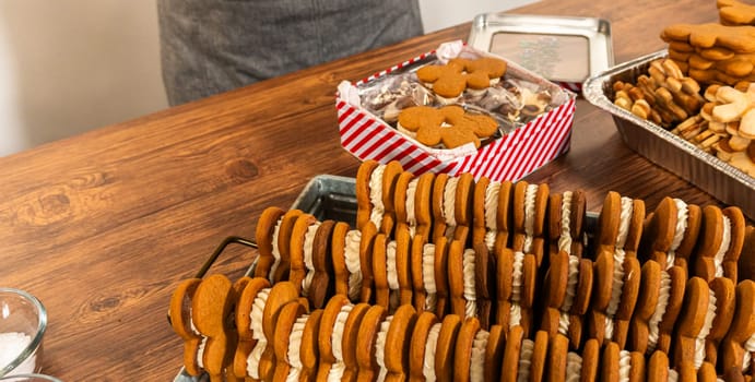 Making gingerbread man cookie sandwiches filled with eggnog buttercream, arrayed on a rustic wooden table, ideal for heartfelt Christmas gifting.