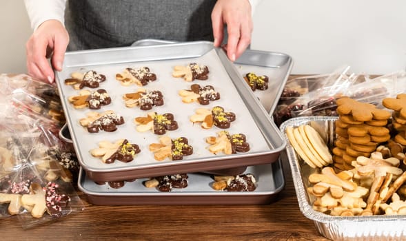 Carefully packaging Christmas cutout cookies, half-dipped in chocolate and presented in clear cellophane wrapping, perfect for festive gifting.