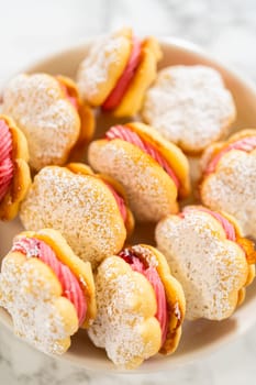A bowl filled with lemon spritz cookie sandwiches, each piped with vibrant cranberry buttercream and dusted with powdered sugar. The cookies have a delicate, buttery texture with a festive touch, making them perfect for holiday baking.