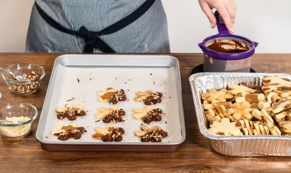 Creating snowflake-shaped cutout sugar cookies, dipped in chocolate, and adorned with crushed pecan nuts, elegantly presented on parchment.