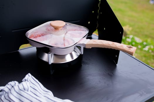 Square pan with wooden handle on stove outdoors.