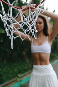 Dynamic scene featuring an athletic woman in a white crop top and skirt posing against a basketball hoop, exuding empowerment and energy in a lush green background
