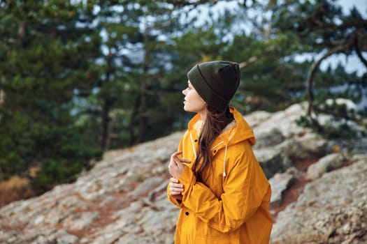 A woman in a yellow raincoat enjoying the breathtaking view of the mountain landscape during a hiking trip