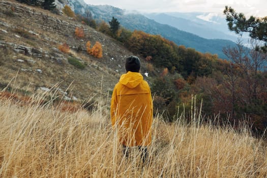 A person in a yellow coat enjoying the serene beauty of nature with majestic mountains in the background