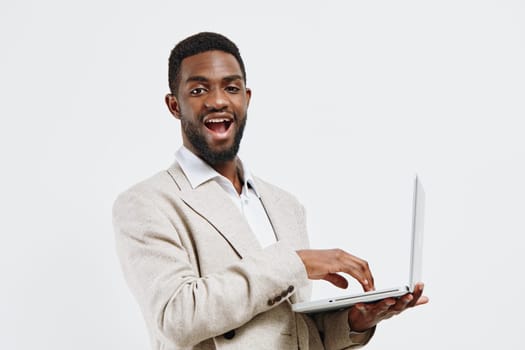 Happy man with a friendly expression holding a laptop computer, dressed in a beige blazer and white shirt, standing against a white studio background, conveying professionalism, confidence, and success, concept: technology and business.