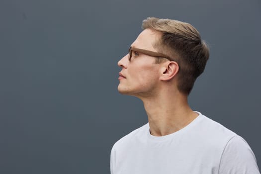 Portrait of a young man with glasses and styled hair wearing casual white t-shirt, facing sideways against a neutral plain background, capturing thoughtful expression and modern lifestyle vibe, studio shot, minimalistic style.