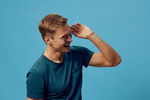 smiling man wear casual blue t-shirt adjust sunglasses on head enjoy positive mood isolated on bright plain blue background digital nomad with relaxed style and cheerful expression Concept: digital nomad