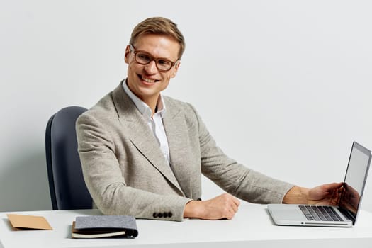 smiling man working with laptop wearing casual business clothes and eyeglasses sitting at desk with digital nomad lifestyle and modern technology concept remote work and productivity background in gray color