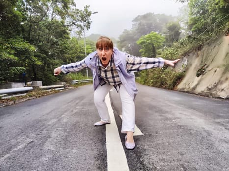 Blonde woman joyfully poses on a deserted road surrounded by fog, showcasing her adventurous spirit as a lifestyle blogger.