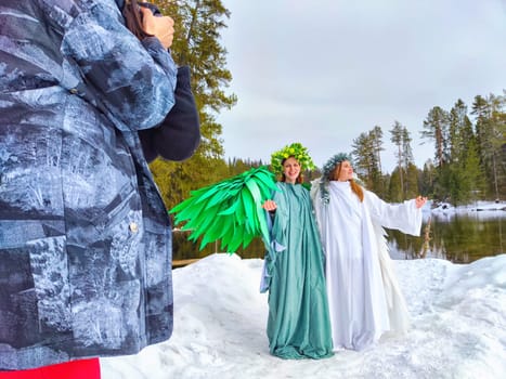 Two girls in elegant dresses express the transition between winter and spring near a serene lake, surrounded by nature.