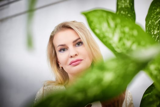 A middle-aged blonde blogger captures a lifestyle moment during a photo shoot in her home, framed by plants.