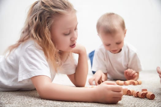 Two children are deeply focused on a wooden game, lying on a soft carpet in a cozy indoor environment in the afternoon.
