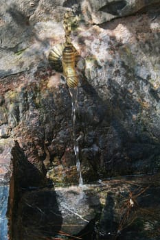 Copper water tap built into the rock, water flows from the tap.