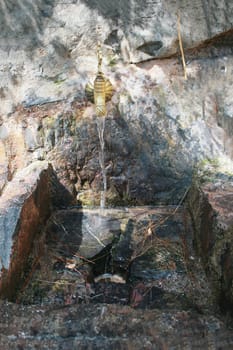 Copper water tap built into the rock, a stream of water flows from the tap. Mountain water source.