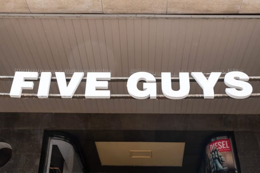 Milan, Italy - April, 08, 2025: Five Guys fast food restaurant storefront sign in bold white letters on metal frame. Street-level entrance exterior view.