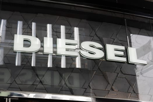 Milan, Italy - April, 08, 2025: Diesel illuminated logo sign on store facade. Brand signage on modern exterior glass with geometric tile reflection details.