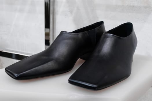 Milan, Italy - April, 08, 2025: Square-toe Phoebe Philo black leather shoes displayed on white sculptural stand inside modern boutique. Sleek footwear detail shot.