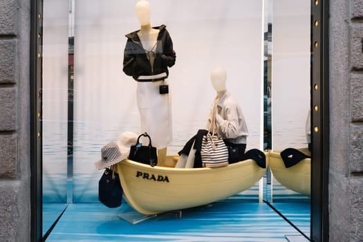 Milan, Italy - April, 08, 2025: Prada store window display in Milan features mannequins in a blue boat with summer fashion. High-end designer retail scene.