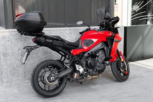 Milan, Italy - April, 08, 2025: Red Yamaha Tracer 9 GT motorcycle parked on urban sidewalk. Sport touring motorbike with top box, black seat, alloy wheels.