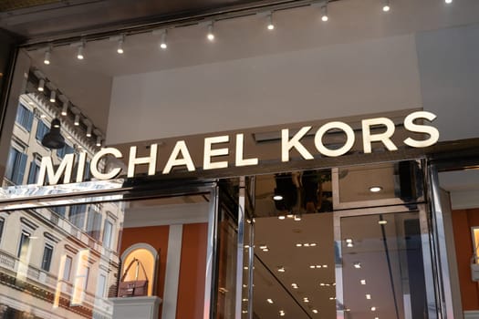Milan, Italy - April, 08, 2025: Michael Kors store entrance with illuminated brand logo and luxury handbag display in Milan. Fashion boutique facade view.