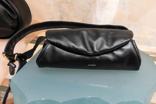 Milan, Italy - April, 08, 2025: Jil Sander black leather shoulder bag with soft folded flap and wide strap. Displayed in Milan fashion boutique interior.