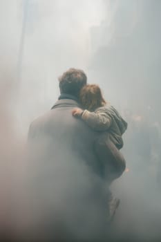 A father carries his young child through a smoky city street, symbolizing protection and survival in a hazardous urban environment. Suitable for themes of pollution, disaster, and resilience