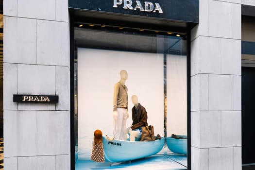Milan, Italy - April, 08, 2025: Prada store window display in Milan features mannequins in a blue boat with summer fashion. High-end designer retail scene.