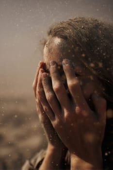 A woman hides her face with her hands amid a sandstorm, dust particles flying through the air. Evokes emotion, survival, and vulnerability. Great for climate, crisis, or emotional impact visuals