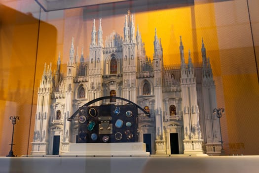 Milan, Italy - April, 08, 2025: Bejeweled designer Louis Vuitton handbag displayed before a detailed Milan Duomo replica. Luxury storefront with golden checkered backdrop.