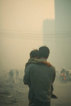 A man carries a young child through thick smog and haze in an urban disaster zone. Strong emotional and environmental narrative suitable for climate, health, or humanitarian themes