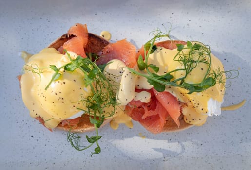Top view of Eggs Royale made with english muffin, oak smoked salmon, a brace of poached hen's eggs & hollandaise sauce and watercress served on blue ceramic tray. use it as your Wallpaper, Poster and Copy space, Selective focus.