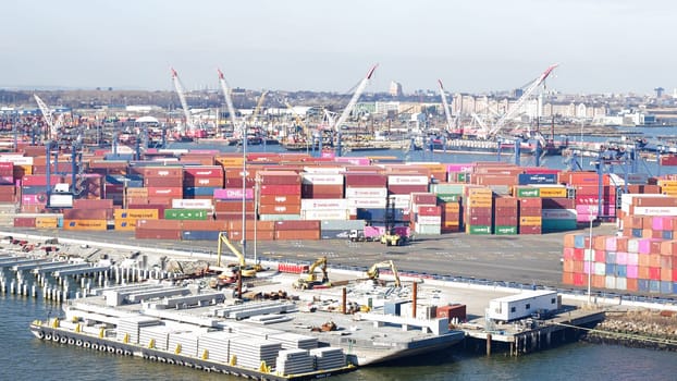 New York NY USA - 09.02.2024: Cargo containers stacked in a shipping yard near the sea with a city in the background.