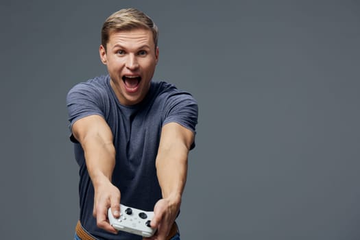 excited young man playing video games holding gamepad controller in casual blue t-shirt standing against gray background focused and joyful digital entertainment concept for gaming and leisure activities