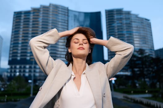 A poised woman in a professional outfit, taking a moment of reflection outdoors amidst contemporary buildings, symbolizing success and ambition in her career.
