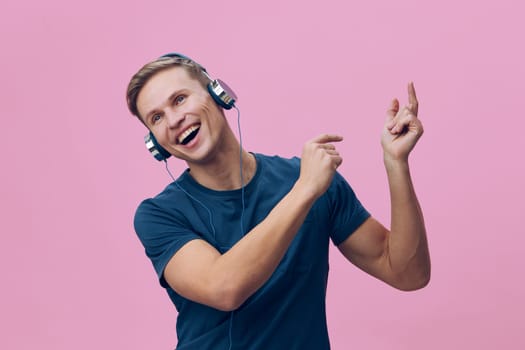 Happy woman wearing headphones expressing joy while dancing, vibrant pink backdrop, casual clothing, youthful energy, music lover, leisure activity, cheerful mood.