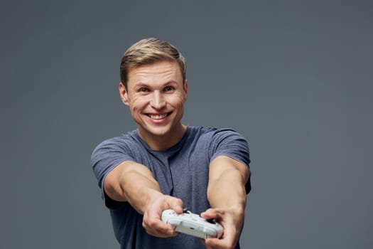 smiling man holding game controller wearing casual t-shirt looking at camera isolated on gray background enjoying digital detox and modern entertainment lifestyle concept with relaxed emotions and minimalist studio setting