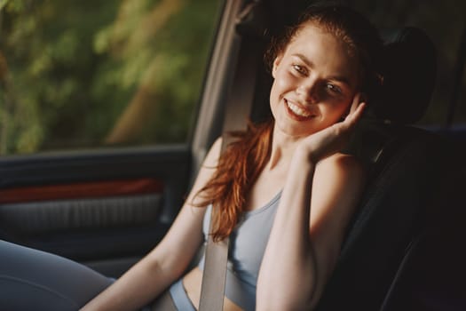 Happy young woman in casual sportswear seated in a car, smiling brightly, emphasizing a joyful and healthy lifestyle reflecting sunny outdoor vibes with natural greenery