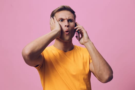concerned man talking on phone with shocked expression wearing casual orange t-shirt on pink background showing emotions of surprise and confusion digital communication and chat with AI concept