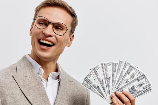 Happy man in formal attire with glasses showing a joyful expression while fanning out cash. The image illustrates financial prosperity, celebration of success, wealth, and positive financial results in a bright professional setting.