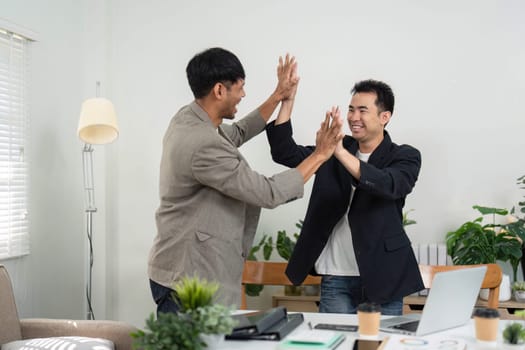 Two business partners engage in a high-five, celebrating a successful collaboration and shared achievements in a bright, modern office environment.
