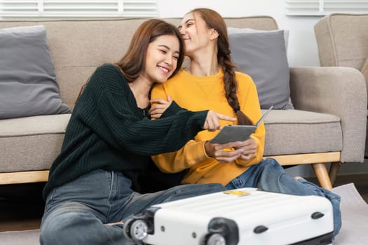 Two women cuddling on the sofa, excited while reviewing travel details together, showcasing their friendship and joy.