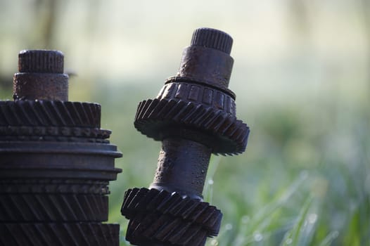 Close up of rusty gears and shafts forming an intriguing outdoor sculpture, showcasing the beauty of decay and repurposing in a natural setting with blurred green grass in the background