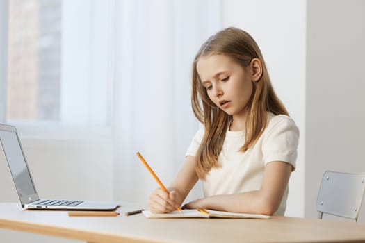 A focused girl in a white shirt writing in her notebook with a pencil, exuding concentration in a bright, minimalistic workspace, perfect for educational themes