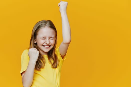 Joyful girl in a yellow shirt raising her fists in celebration against a bright yellow backdrop, embodying happiness and success Perfect for themes of achievement and positivity