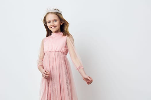 A cheerful young girl in a light pink dress with sheer sleeves, wearing a delicate crown, depicting happiness and innocence against a minimalistic white backdrop, ideal for fashion and celebration themes