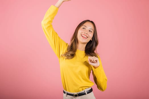 Asian young woman dancing with inspired face expression and raising hands up, Portrait of happy female model jocund in sneakers dancing, studio shot isolated on pink background, Time to relax